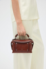 Profile view of model wearing the Oroton Mica Burnished Leather Mini Bowler in Dark Chestnut and Smooth, vegetable-tanned leather for Women .