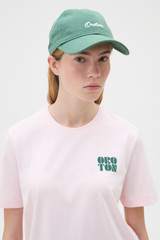 Profile view of model wearing the Oroton Oroton Script Cap in Racing Green and 100% cotton canvas fabric for Women .